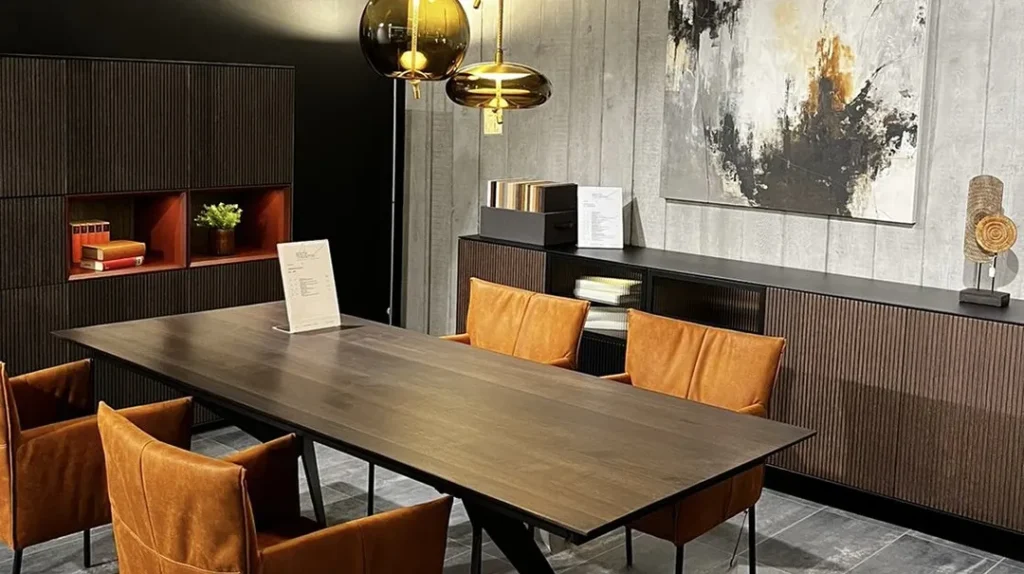 A modern dining room with a dark wood table, six brown leather chairs, pendant lights, abstract wall art, and shelves with books and decor on a grey textured wall.