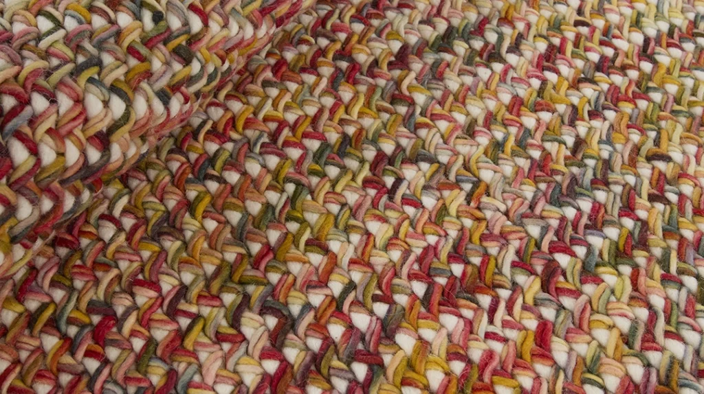 Close-up of a colourful, chunky knitted fabric with interwoven strands of red, yellow, green, and white yarn creating a textured, plaited pattern.