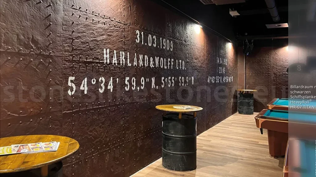 Industrial-themed bar with dark metal-textured walls, white stencilled text/numbers, and round tables made from metal barrels. Pool tables and hardwood flooring are visible, with spotlights illuminating the space.