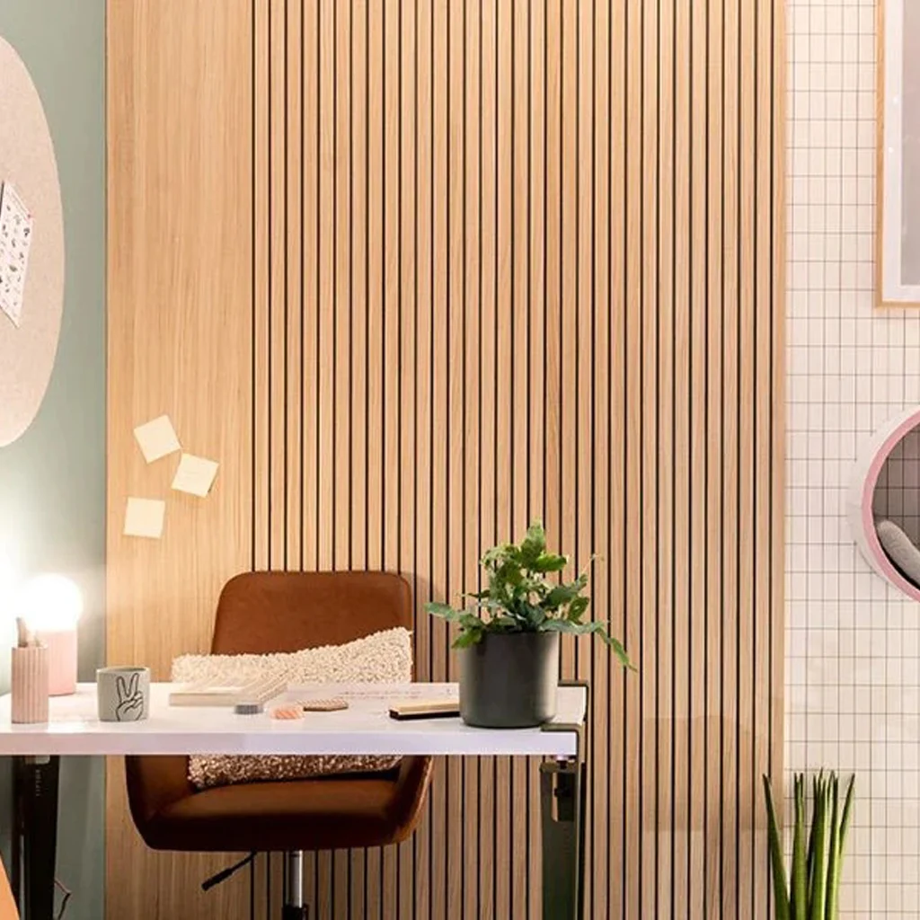 A modern workspace with a brown chair, a white desk holding a potted plant and stationery, light wooden slat wall, green feature wall, and round decor elements including a mirror and pin board with sticky notes.