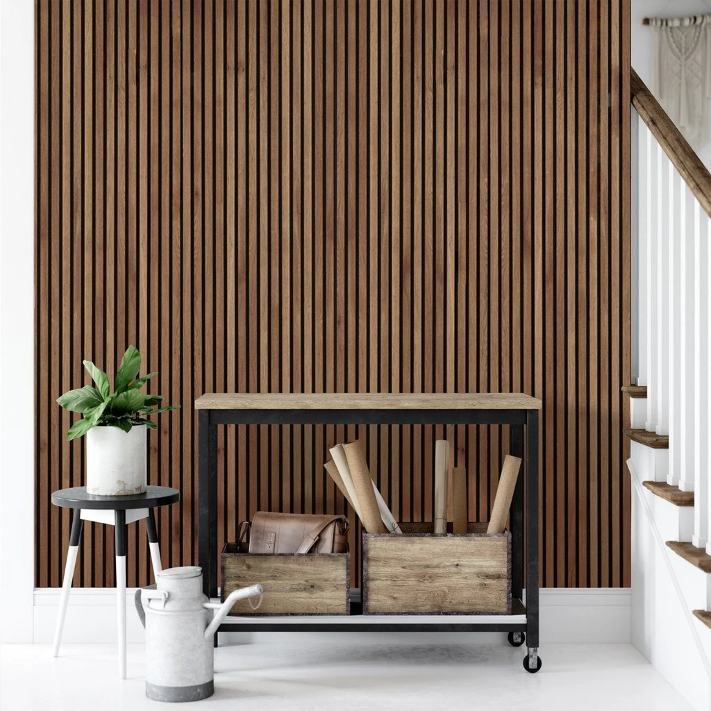 A modern hallway with a slatted wooden feature wall, a small black table holding a potted plant, a wooden console table with books and drawers, and a white staircase with wooden steps. A metal watering can sits on the floor.