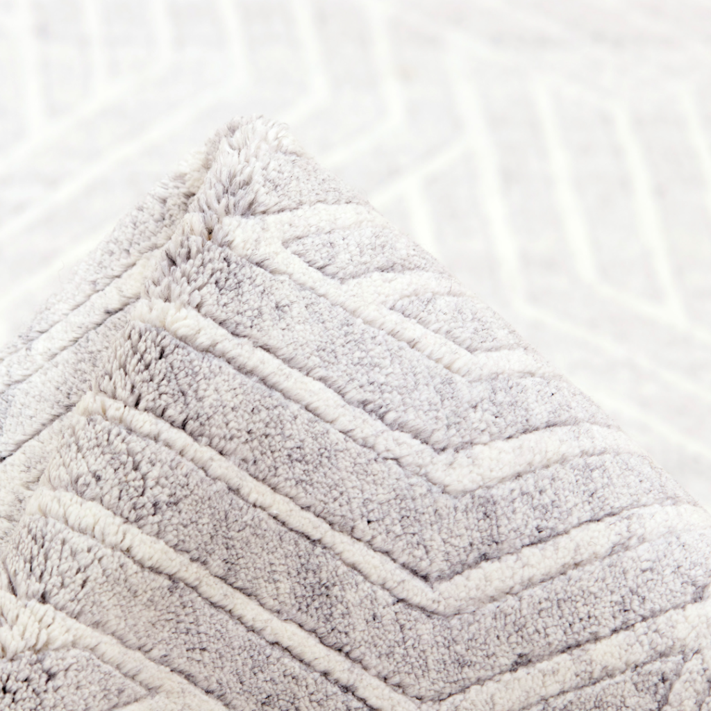 Living Room Rug Ideas. A close-up of a soft, textured cushion with a chevron pattern in light beige and cream tones, set against a matching patterned background.