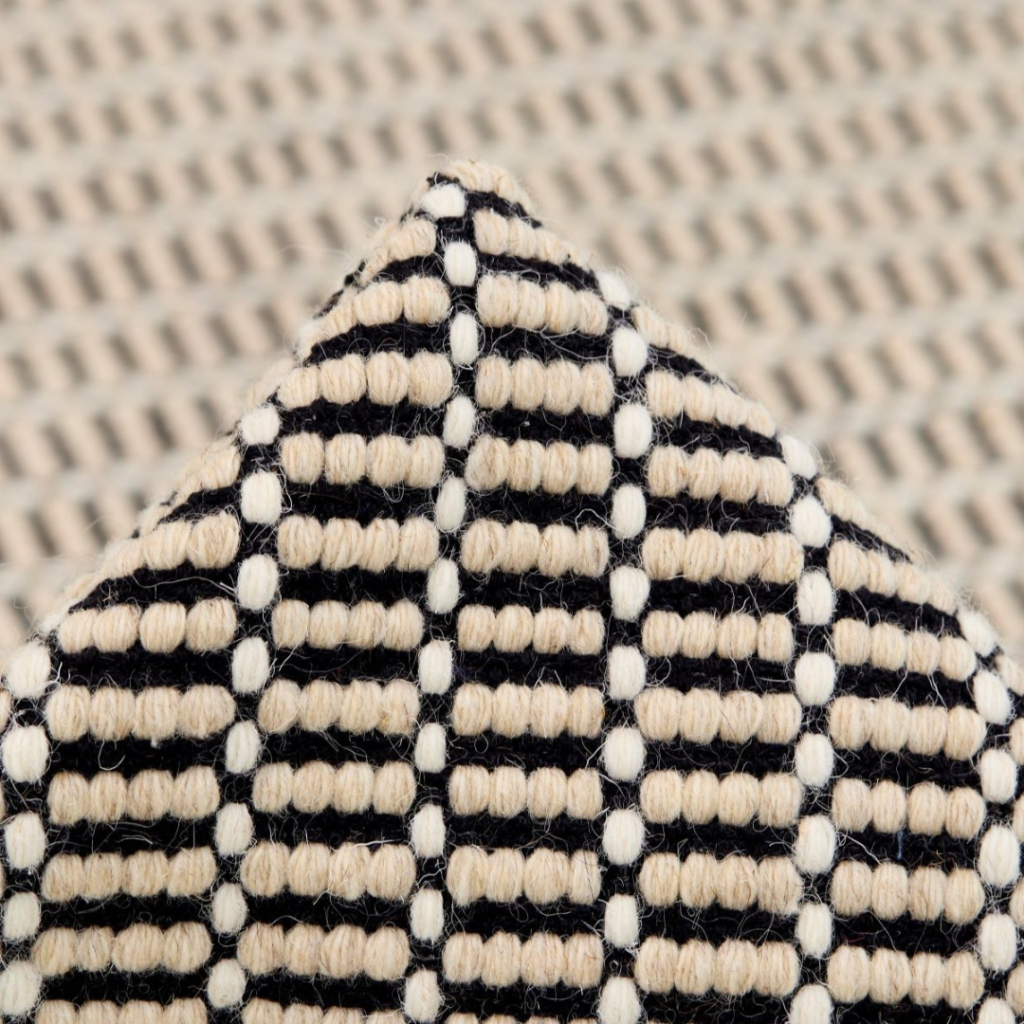 Dining Room Rug Ideas. Close-up of a textured fabric with a geometric pattern of black and beige horizontal and vertical lines forming small rectangles, creating a grid-like appearance. The background shows a blurred version of the same pattern.