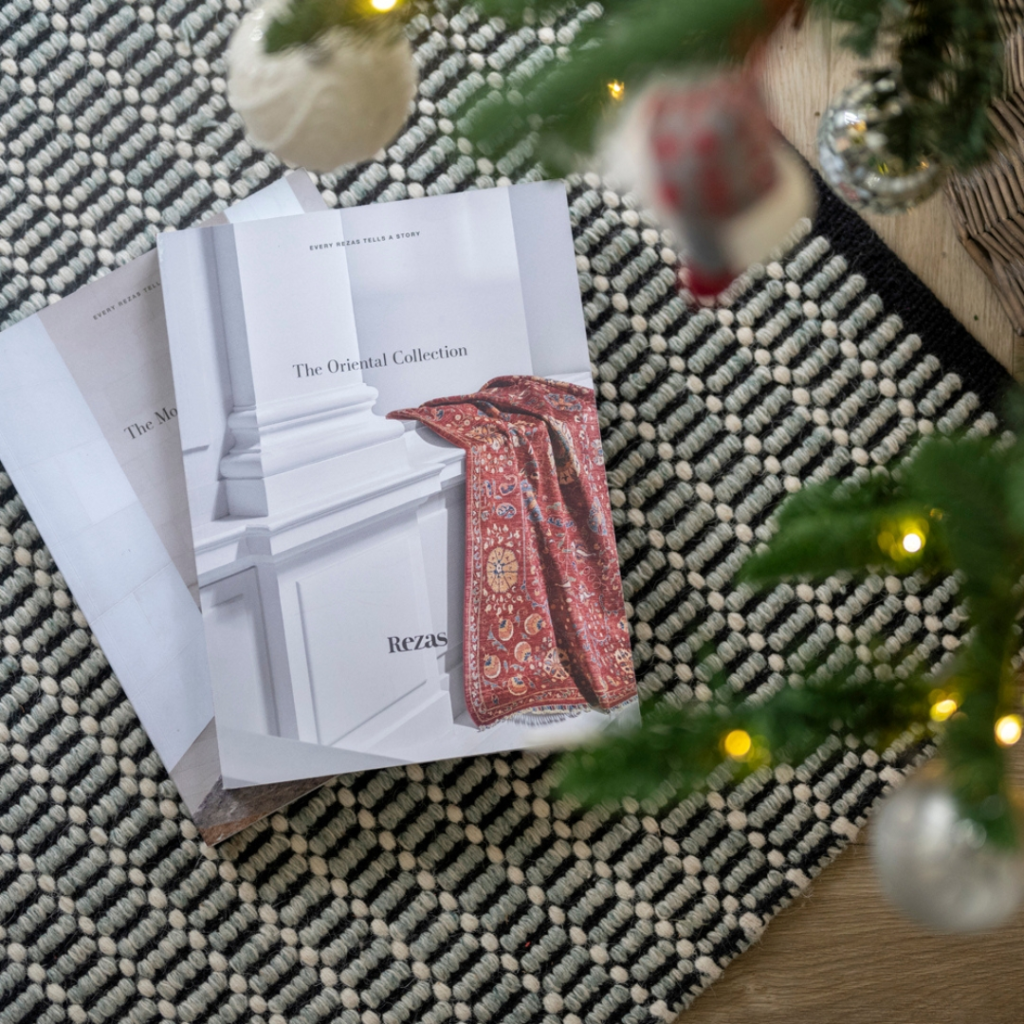 Two magazines, one titled The Oriental Collection, lie on a patterned black-and-white rug near a Christmas tree decorated with baubles and lights.
